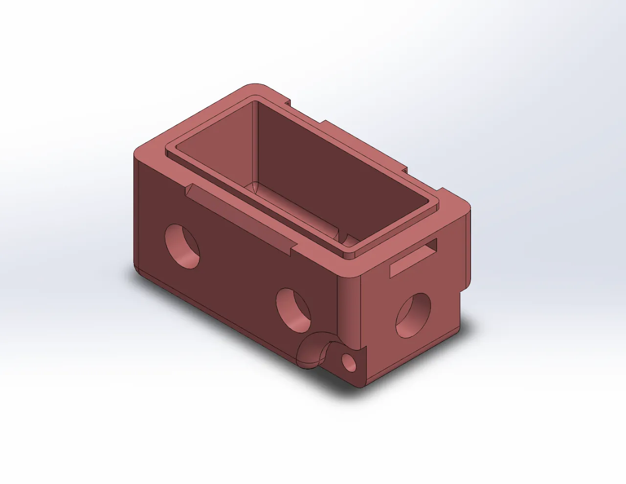 SolidWorks model of an open-top rectangular enclosure, shaded muted red, on a light background. A stepped lip runs around the inside of the opening. The long side wall has two round openings and the end wall has one. There are small rectangular slots near the top edges and a small rounded boss with a hole at one bottom corner.